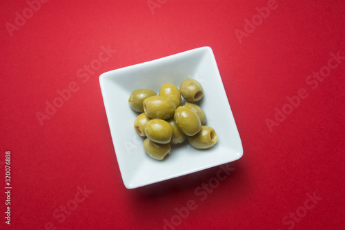 Olives stuffed with pieces of red pepper, in a white bowl, on a red background.