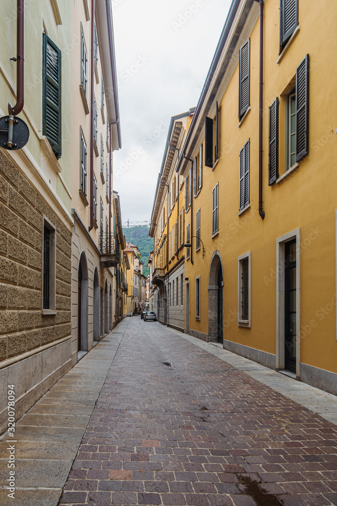 View of a narrow, empty street with pastel colorful facades of houses in Como, Italy.