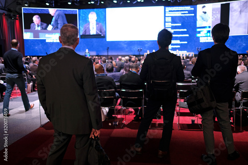 Photography Audience members at a conference follow the presentation on stage