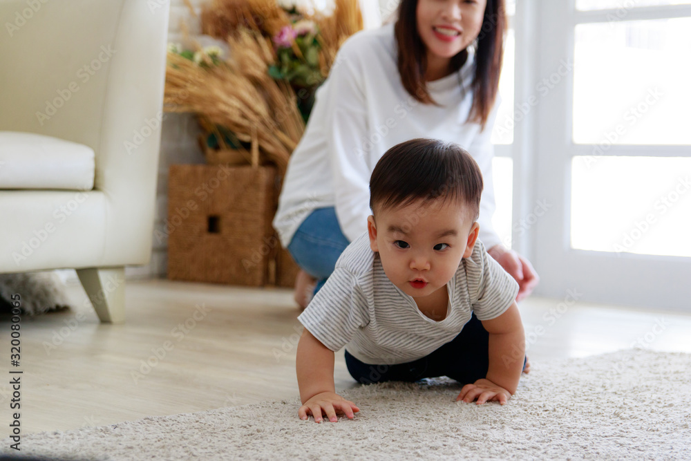 Asian baby crawl with determination. Mother looks at the child's development with pride. Her face is smiling happy.White tone and copy space Asian baby crawl with determination. Mother looks at the child's development with pride. Her face is smiling happy.White tone and copy space