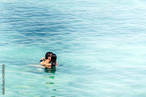 Young strong man in love hugging and embracing girlgriend in a bikini suit in the sea. Beautiful couple in the sea.