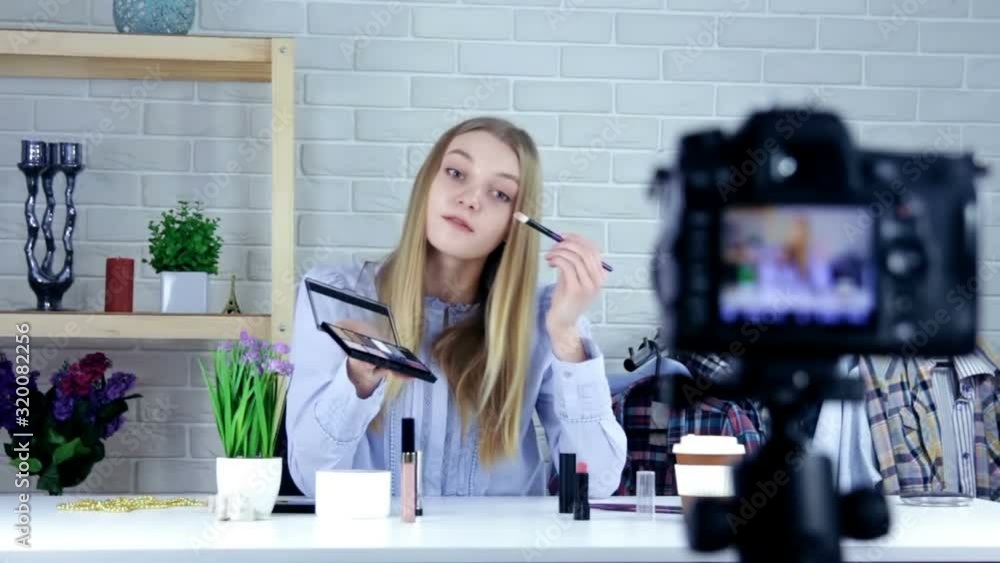 Smiling woman or beauty blogger with eye shadow brush, mirror and camera recording makeup tutorial video at home - blogging, technology, videoblog, makeup and people concept Smiling woman or beauty blogger with eye shadow brush, mirror and camera recording makeup tutorial video at home - blogging, technology, videoblog, makeup and people concept