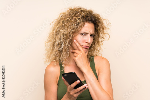 Young blonde woman with curly hair using mobile phone thinking an idea