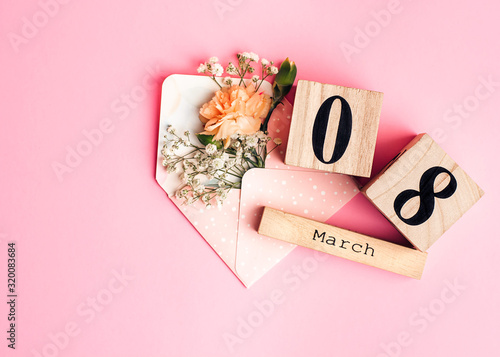 Womens day composition. 8 march wooden calendar with flowers in an envelope on the pink background. Copy space, top view