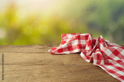 Empty wooden table with red checked tablecloth over green bokeh background. Spring and easter mock up for design.