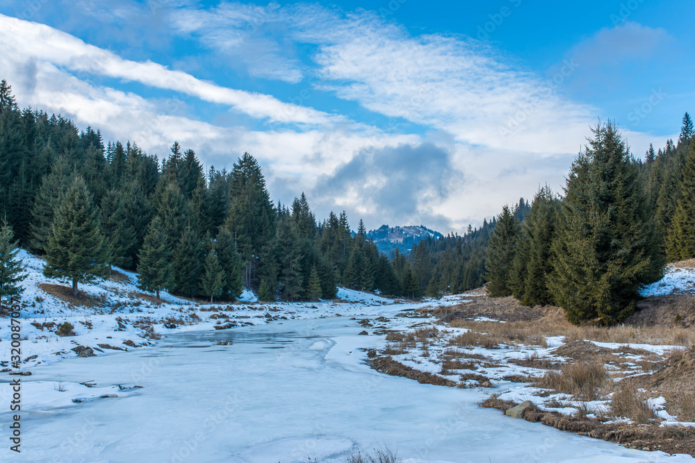 Frozen river on a cold winter day in the Carpathian mountains, Romania , blue sky with white clouds.