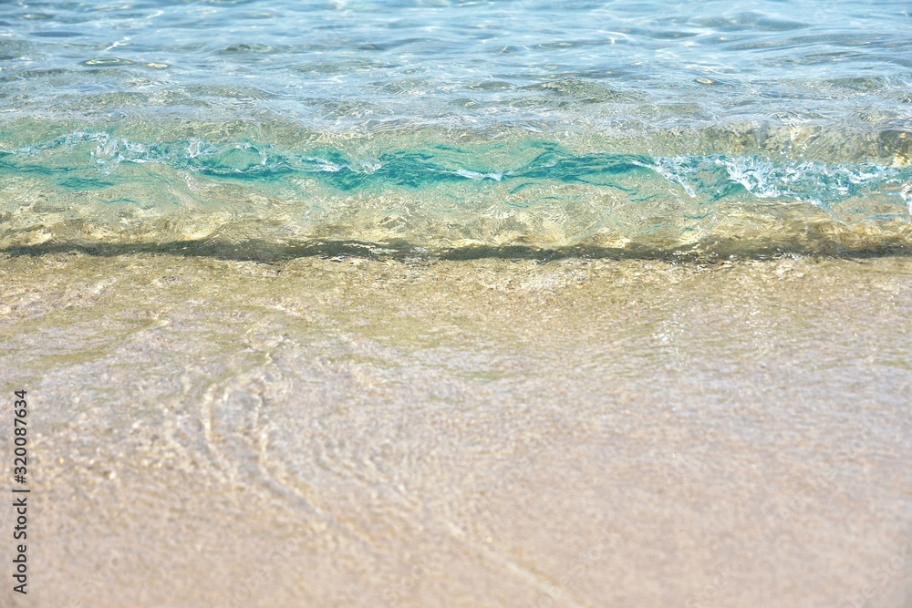 Sea coast with a beautiful soft wave. Transparent blue sea wave with white foam on a clean sandy shore, selective focus. turquoise ocean water. Summertime. Empty sand beach with soft wave background.