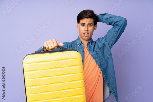 Man over isolated purple background in vacation with travel suitcase and surprised © luismolinero