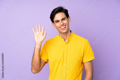 Man over isolated purple background saluting with hand with happy expression