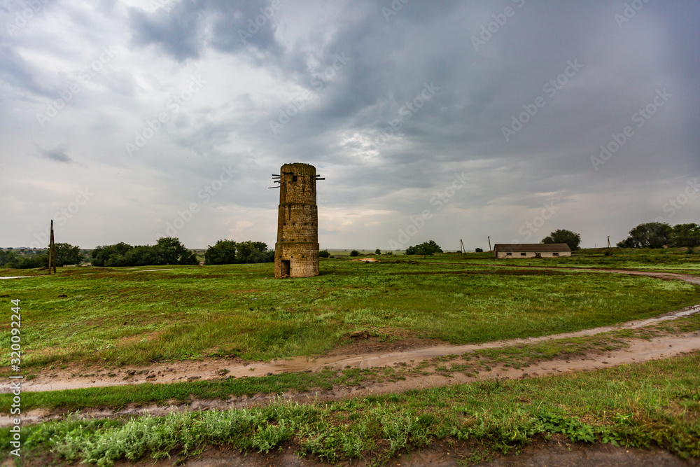 old brick tower standing on the outskirts of the village by a dirt road after rain