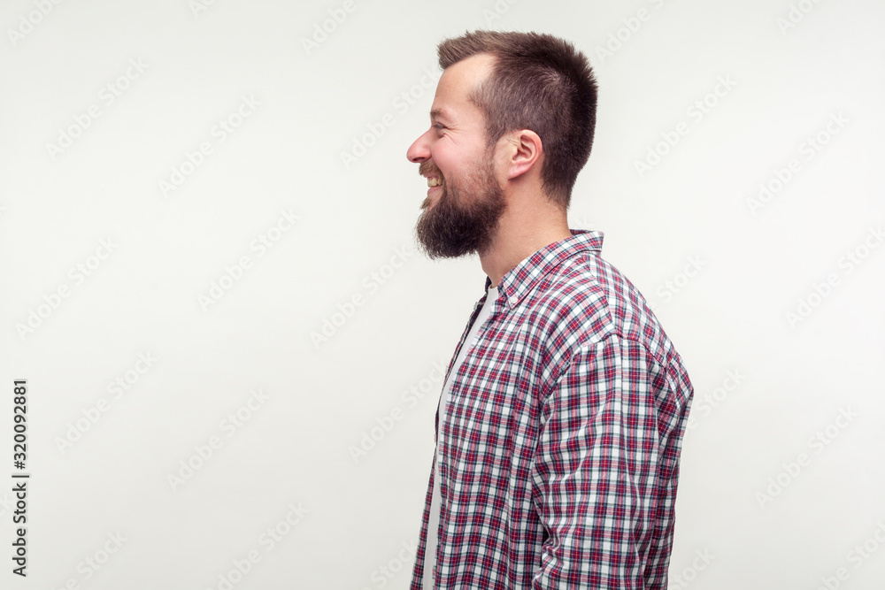 Side view portrait of happy bearded man in casual plaid shirt smiling sincerely, satisfied contented with life, empty place for ad text, copy space. indoor studio shot isolated on white background Side view portrait of happy bearded man in casual plaid shirt smiling sincerely, satisfied contented with life, empty place for ad text, copy space. indoor studio shot isolated on white background