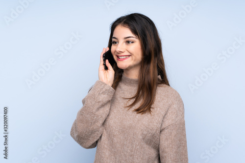 Young brunette woman wearing a sweater over isolated blue background keeping a conversation with the mobile phone