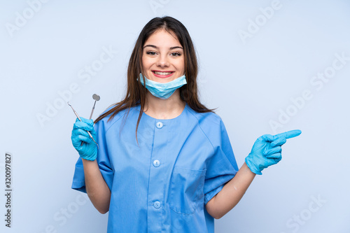 Woman dentist holding tools over isolated blue background pointing finger to the side photo
