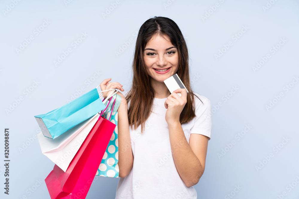 Young brunette woman over isolated blue background holding shopping bags and a credit card Young brunette woman over isolated blue background holding shopping bags and a credit card