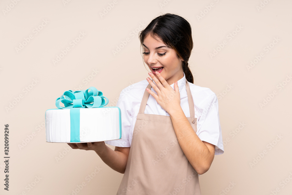 Pastry chef woman holding a big cake over isolated background with surprise and shocked facial expression Pastry chef woman holding a big cake over isolated background with surprise and shocked facial expression