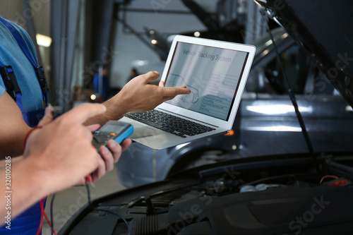 Fotografie Mechanics with laptop doing car diagnostic at automobile repair shop, closeup