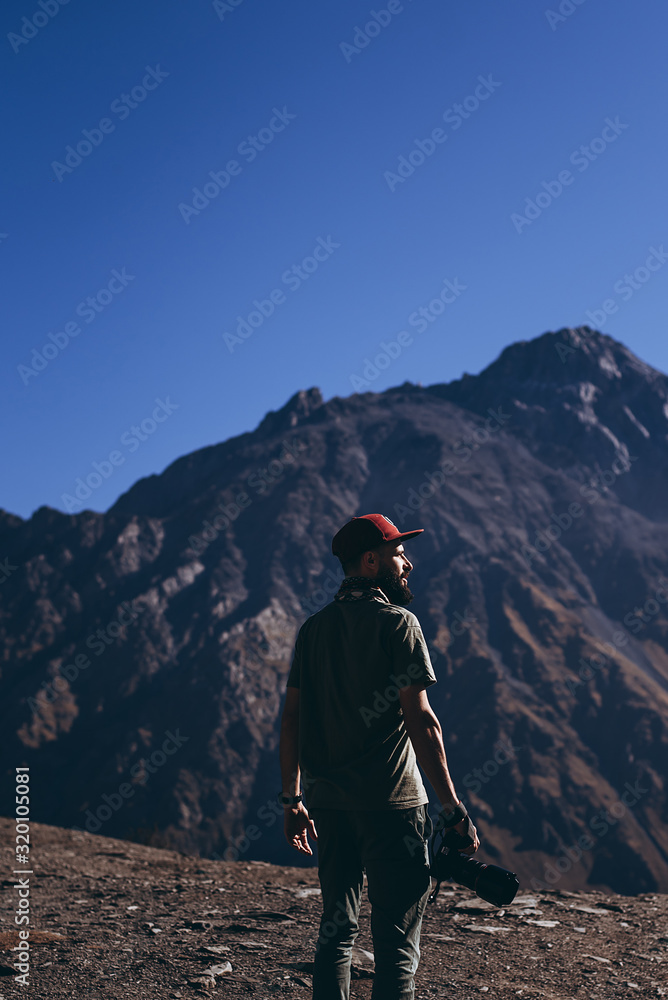 stylish bearded man with camera in hands on top of Georgian mountains: nature photographer traveler taking photo of beautiful landscape from top of the mountain stylish bearded man with camera in hands on top of Georgian mountains: nature photographer traveler taking photo of beautiful landscape from top of the mountain