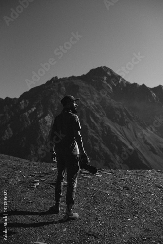 stylish bearded man with camera in hands on top of Georgian mountains: nature photographer traveler taking photo of beautiful landscape from top of the mountain
