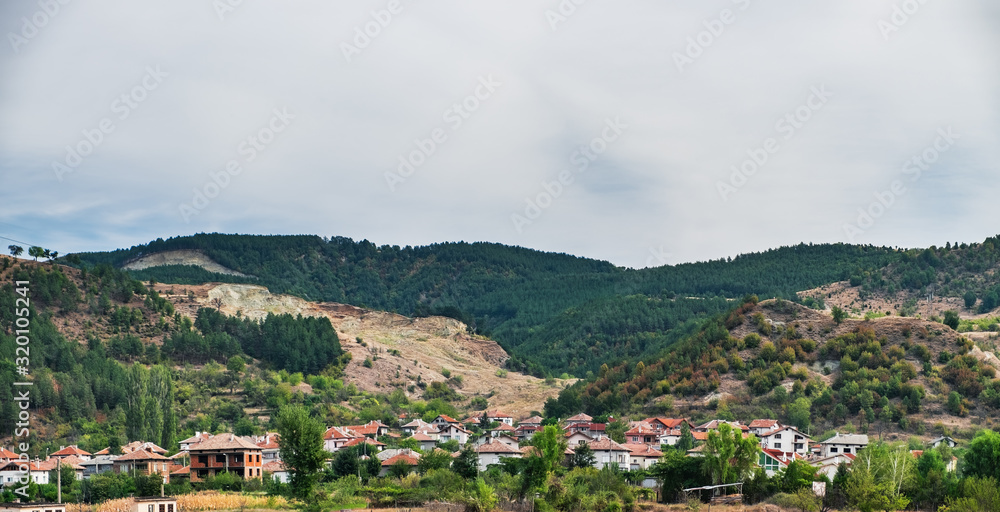 Typical natural rural landscape in Bulgaria in summertime, Bulgarian traditional village with red roofs, gardens and vineyards, hills on the horizon