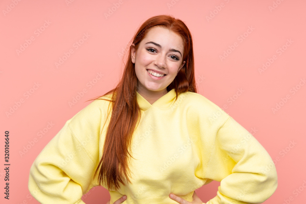 Redhead teenager girl over isolated pink background posing with arms at hip and smiling Redhead teenager girl over isolated pink background posing with arms at hip and smiling