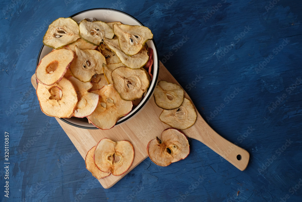 Fototapeta premium Organic Apple and pear chips (slices) lie on the kitchen Board on a blue background. Dried Apple and pear slices are a healthy vegetarian fruit snack or cooking ingredient. Healthy food concept.