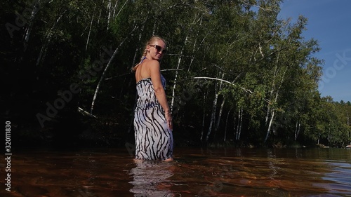 Fototapeta Naklejka Na Ścianę i Meble -  Woman walk on water on pier in sunglasses and a boho silk shawl. Girl rest on flood wood underwater dock. The pavement is covered with water in lake.
