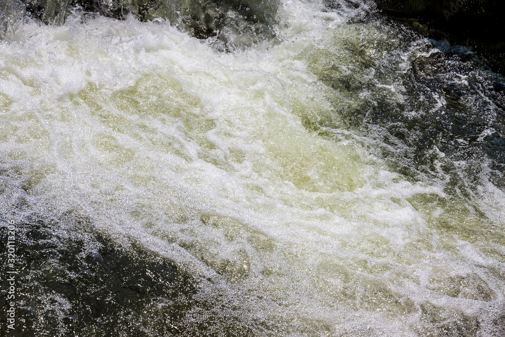 A steep stream of water in a mountain river. Water texture with foam_