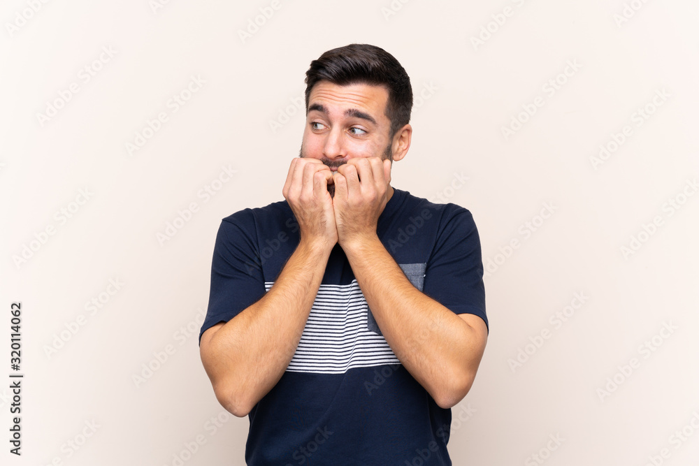 Young handsome man with beard over isolated background nervous and scared putting hands to mouth Young handsome man with beard over isolated background nervous and scared putting hands to mouth