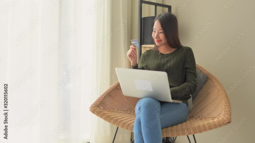 A young Asian woman balances a laptop on her knees while inputting her credit card information. Copy space A young Asian woman balances a laptop on her knees while inputting her credit card information. Copy space
