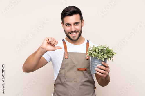 Gardener man holding a plant over isolated background proud and self-satisfied