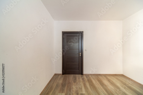 Closed wooden door in empty room  wooden flooring.  White walls