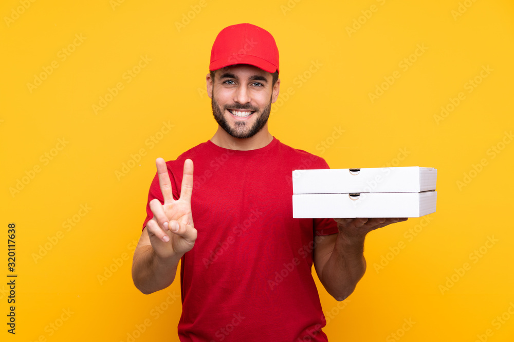pizza delivery man with work uniform picking up pizza boxes over isolated yellow background smiling and showing victory sign pizza delivery man with work uniform picking up pizza boxes over isolated yellow background smiling and showing victory sign