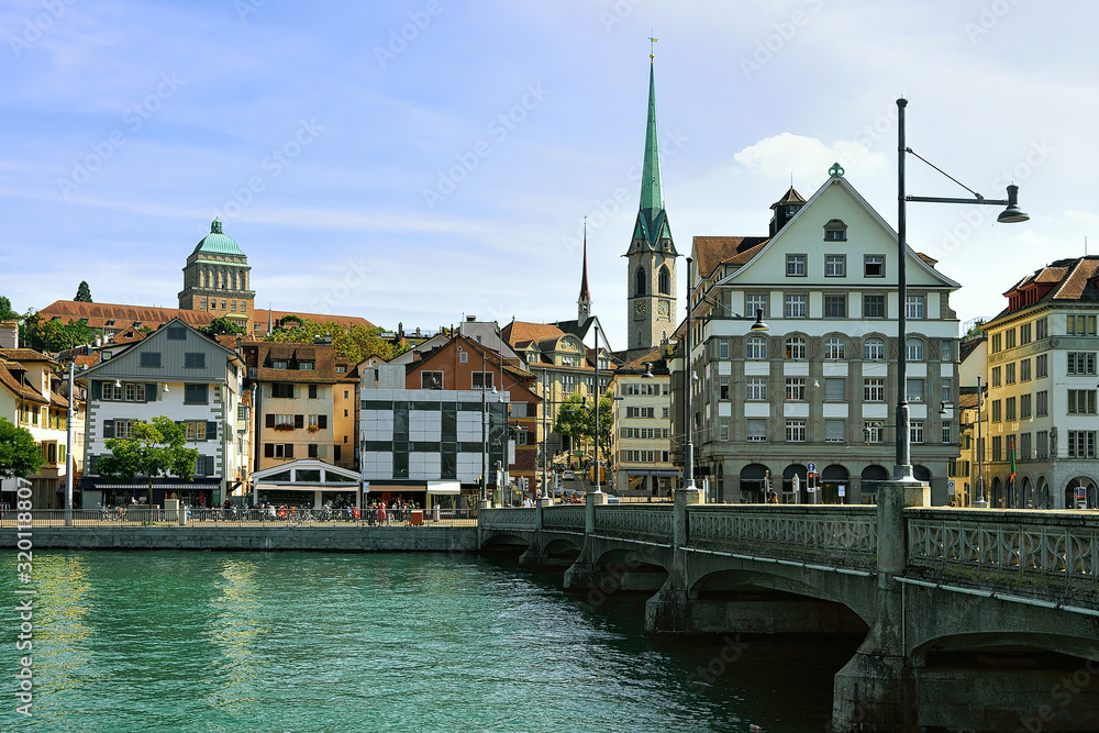 Fraumunster Church and Munsterbrucke bridge at Limmat River quay in the city center of Zurich, Switzerland. People on the background