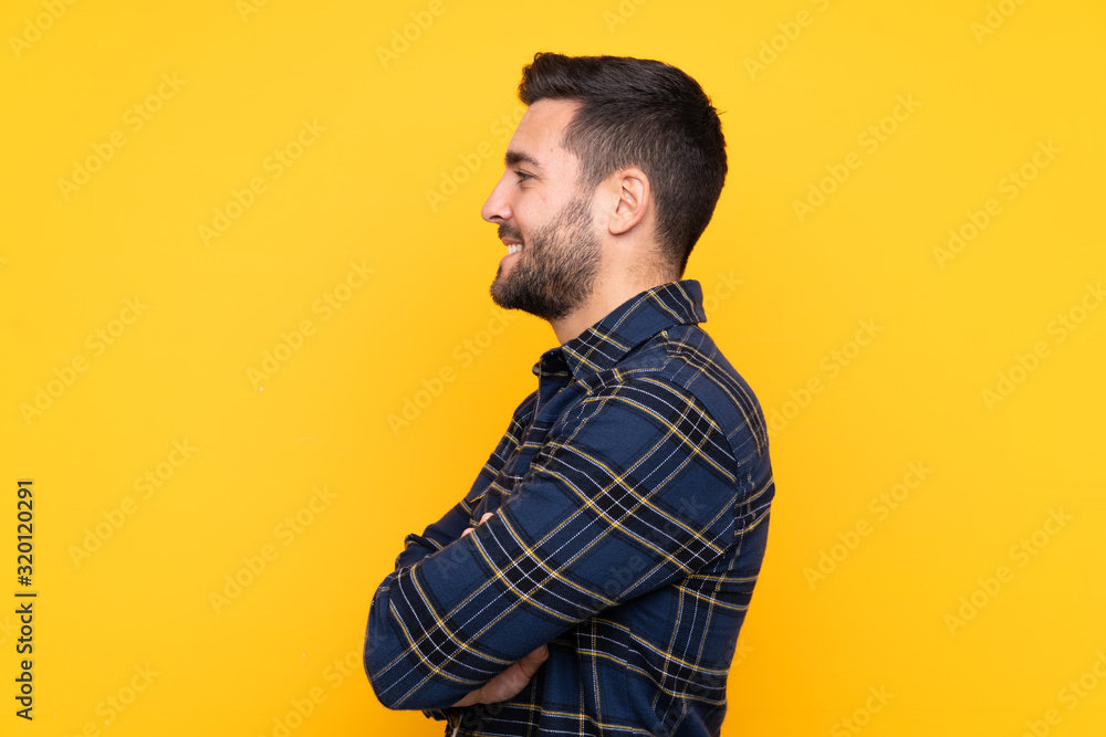 Fototapeta premium Young handsome man with beard over isolated yellow background in lateral position