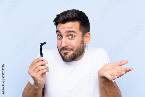 Young handsome man shaving his beard over isolated background making doubts gesture while lifting the shoulders
