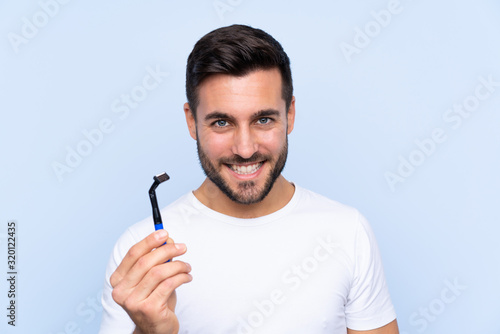 Young handsome man shaving his beard over isolated background with happy expression