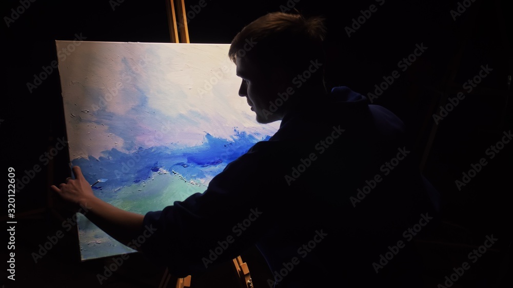 Fototapeta premium Artist copyist paint seascape with ship in ocean. Craftsman decorator draw as boat sail on blue sea with acrylic oil color. Draw finger, brush, knife palette. Canvas, easel in studio, indoor.