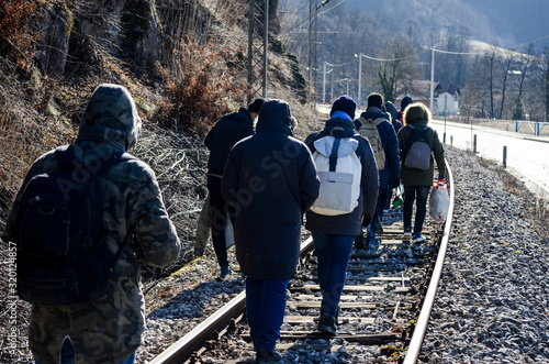 Group of migrants walking along railway tracks. Balkan route. Rear view of men walking on railway tracks in spring. Migrant and refugee walking to EU. Migration in Bosnia and Herzegovina. Syria, Iraq, photo