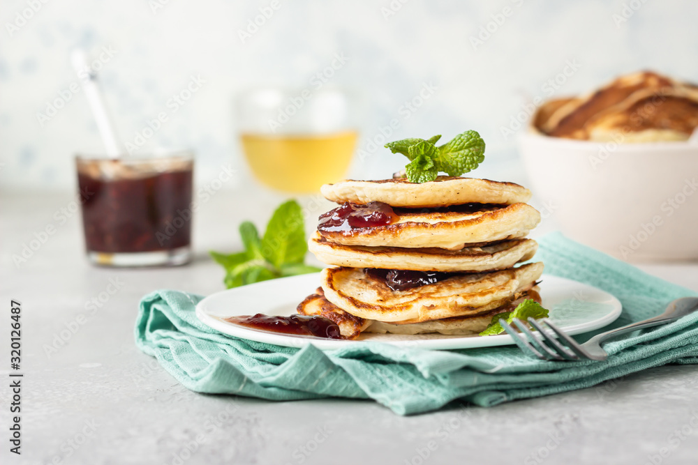 Pancakes with red berry jam and mint, herbal tea. American cuisine. Perfect idea for breakfast. Light grey stone background. Pancakes with red berry jam and mint, herbal tea. American cuisine. Perfect idea for breakfast. Light grey stone background.