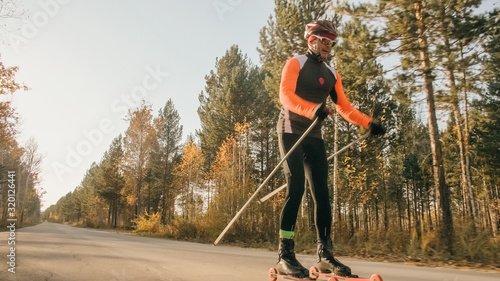 Training an athlete on the roller skaters. Biathlon ride on the roller skis with ski poles, in the helmet. Autumn workout. Roller sport. Adult man riding on skates. © ivandanru