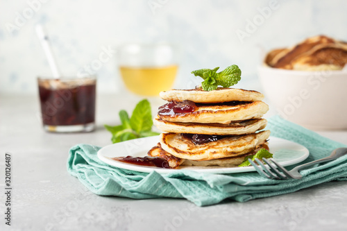 Pancakes with red berry jam and mint, herbal tea. American cuisine. Perfect idea for breakfast. Light grey stone background.
