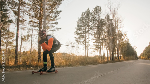 Training an athlete on the roller skaters. Biathlon ride on the roller skis with ski poles, in the helmet. Autumn workout. Roller sport. Adult man riding on skates. © ivandanru