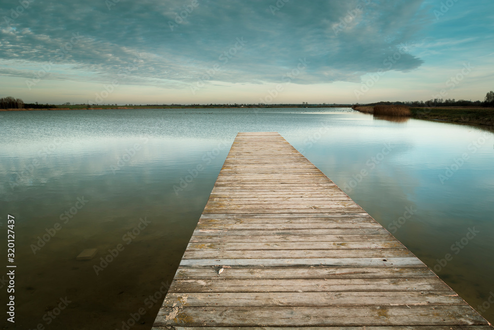 Long wooden bridge on the calm lake, evening clouds on the sky