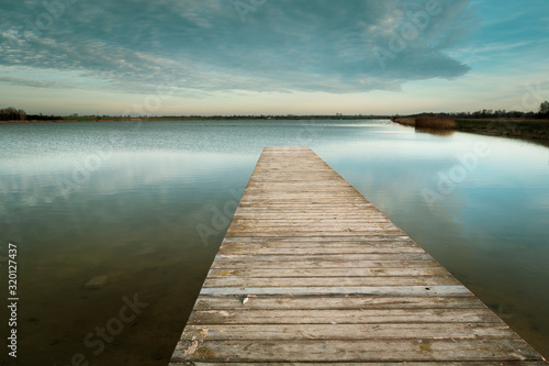 Long wooden bridge on the calm lake, evening clouds on the sky