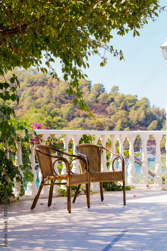 Two wicker chairs on the background of the garden and sea. Seaside chair, relax in the shade at the resort