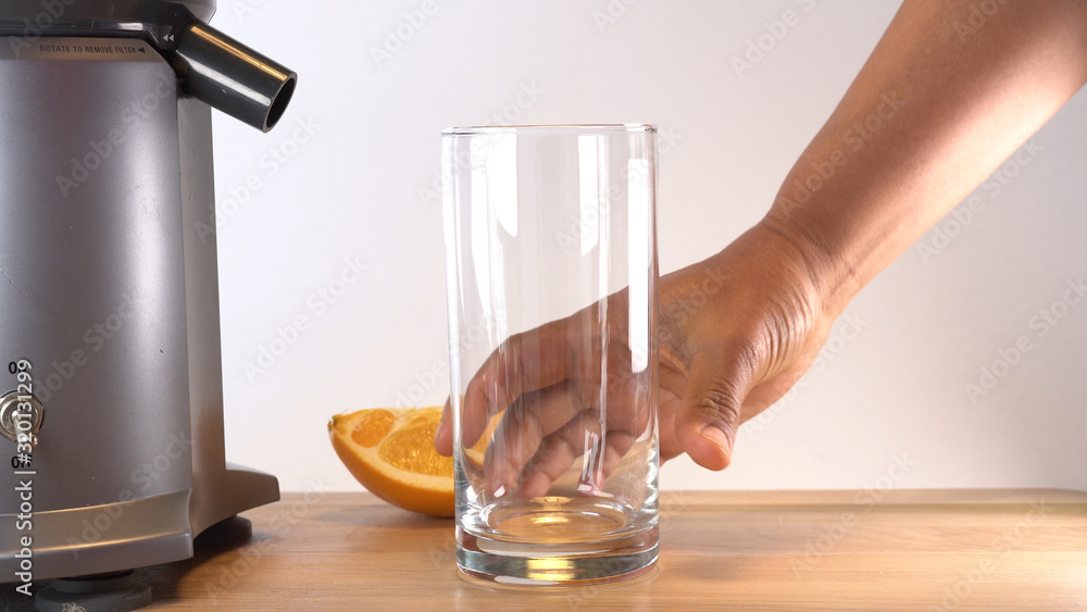 hand reaching to an empty glass next to a juicer and sliced orange hand reaching to an empty glass next to a juicer and sliced orange
