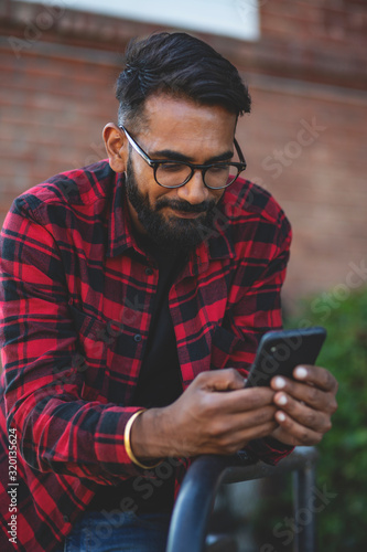 Handsome young man, outdoor. Indian man is texting a message on a cell phone.