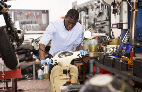 Confident man worker repairing motorcycle in workshop