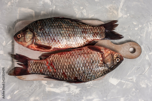 Two fresh crucian fish lies on a white wooden cutting board on a light gray background. Top view