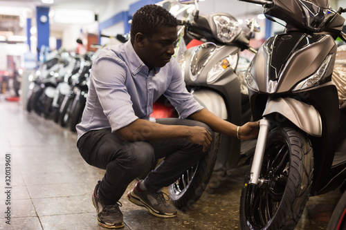 Afro american man is shopping and choosing new motobike in moto store